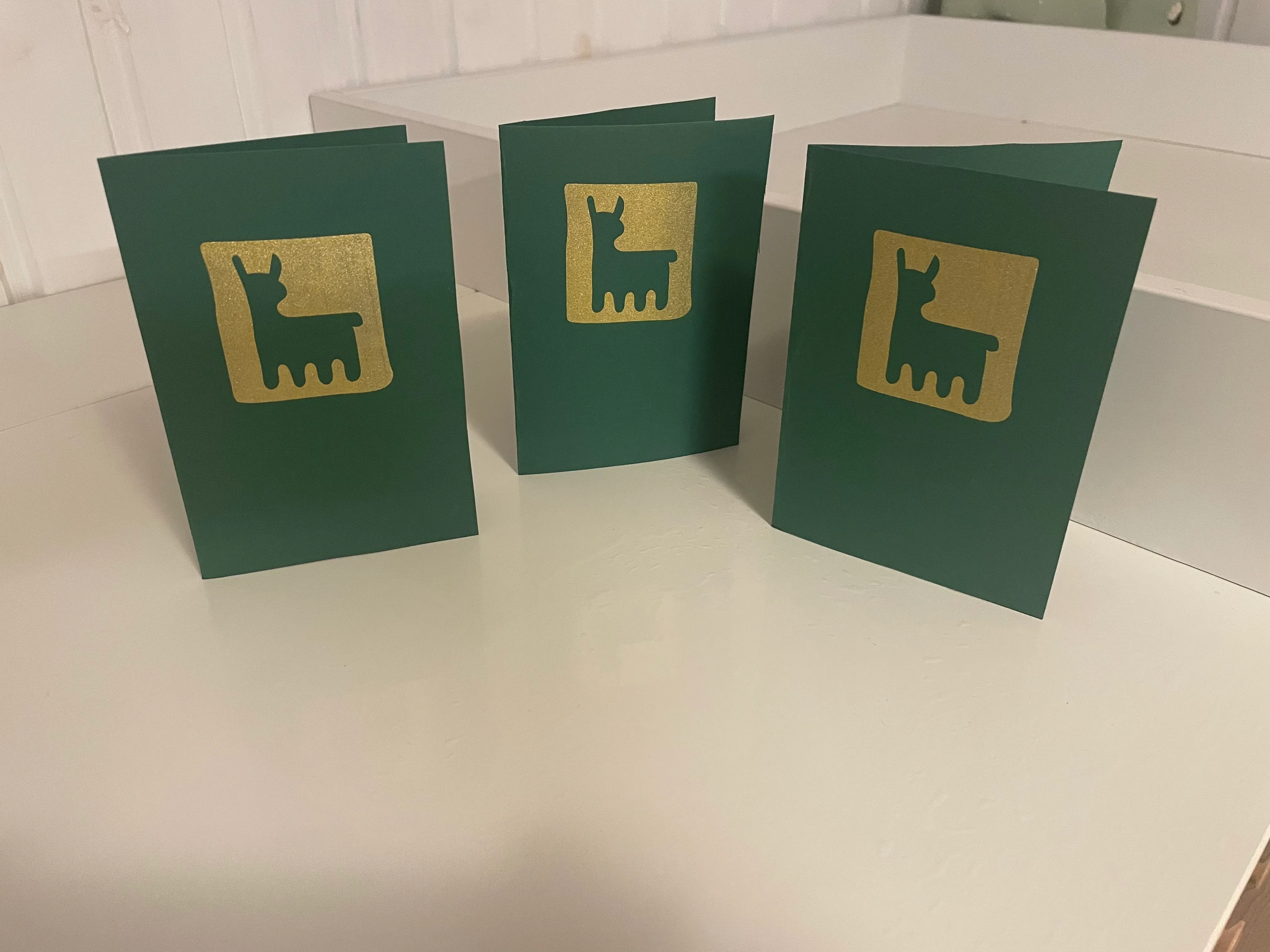 Drei dunkelgrüne Klappkarten mit goldenem Quadrat und ausgespartem Alpaka-Motiv